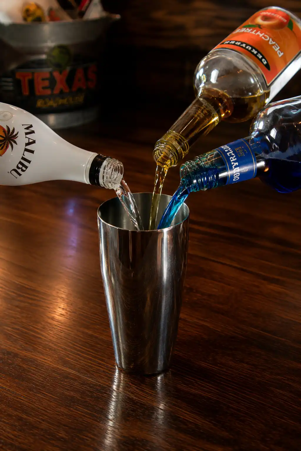 Coconut rum, peach schnapps, and blue curaçao being poured into a cocktail shaker